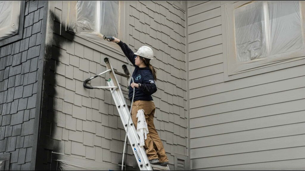 A lady roe paint professional spray painting the exterior part of the house